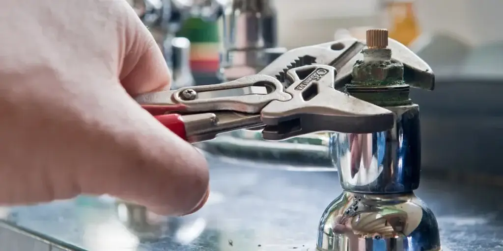 Hand using an adjustable wrench to tighten a faucet valve.