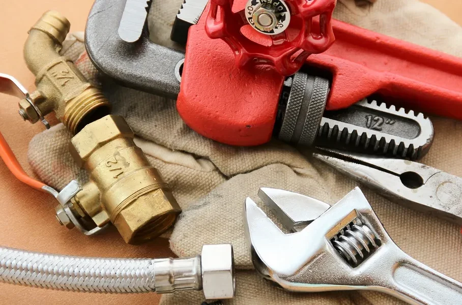 Plumbing tools including wrenches, pliers, and valves on a cloth surface.
